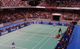 Ein spannendes Tennismatch in einer vollen Halle, mit Spielern, die sich auf dem Platz gegenüberstehen.