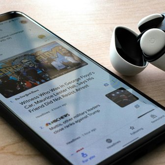 Das Bild zeigt ein Smartphone mit aktuellen Nachrichten und ein Paar kabelloser Kopfhörer, die auf einem Tisch liegen.