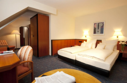 Ein gemütliches Hotelzimmer mit zwei Betten, einem Schreibtisch und einer modernen Lampe, die eine warme Atmosphäre schafft.