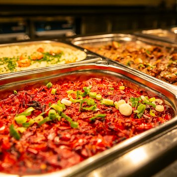 Eine Auswahl an buntem, köstlichem Essen in einer Buffet-Anordnung, mit frischen Kräutern und verschiedenen Beilagen.