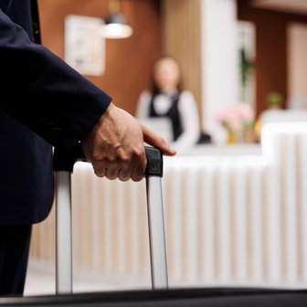 Ein Geschäftsmann mit einem Koffer steht in der Hotellobby, während eine Empfangsdame im Hintergrund arbeitet.