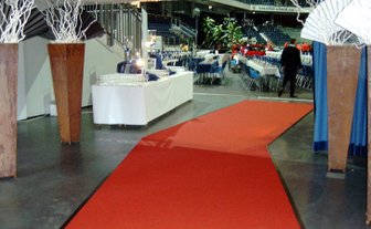 Ein roter Teppich führt durch eine festlich dekorierte Halle mit Tischen und Stühlen für eine Veranstaltung.