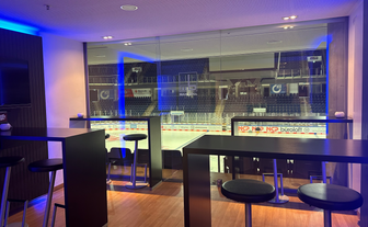 Ein stilvoller Lounge-Bereich mit Möbeln und in abgedunkelt-blauen Farbtönen, der eine klare Sicht auf das Eisstadion und die Zuschauerplätze ermöglicht.