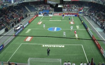 Ein Blick auf das Spielfeld, umgeben von Zuschauern, die die aufregende Atmosphäre eines Hallenfußballspiels genießen.