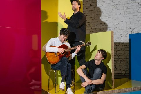 Drei Bandmitglieder von AnnenMayKantereit vor bunter Kulisse