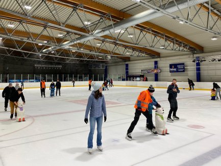 Eisläufer in warmer Kleidung bewegen sich über die glatte Fläche, während ein Mitarbeiter die Sicherheit überwacht.
