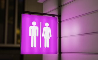 Ein leuchtendes, lila Schild zeigt die Symbole für Männer und Frauen, das auf eine Toilette hinweist.