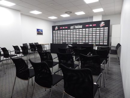 Ein Konferenzraum mit mehreren schwarzen Stühlen und einer Wand voller Sponsorenlogos der Ice Tigers.