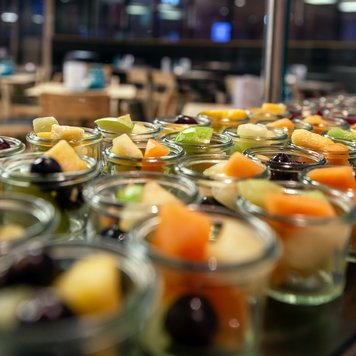 Eine Vielzahl von kleinen Gläsern mit buntem Obstsalat, darunter Melonen, Trauben und Ananas, auf einem Tisch in einem Restaurant.