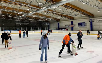Eisläufer in warmer Kleidung bewegen sich über die glatte Fläche, während ein Mitarbeiter die Sicherheit überwacht.