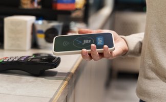 Eine Person hält ein Smartphone mit einem NFC-Symbol, bereit zur kontaktlosen Zahlung an einem Kassenterminal.