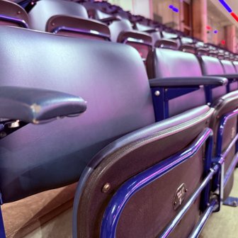 Ein leerer, gepolsterter Sitz in einem Stadion, der auf die bevorstehende Veranstaltung hinweist, umgeben von weiteren leeren Plätzen.
