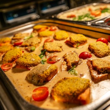 Ein Blech mit knusprigem Fischfilet, garniert mit Kirschtomaten und einer cremigen Sauce, serviert in einem Buffet-Stil.
