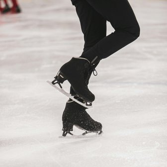 Ein Eiskunstläufer zeigt eine elegante Pose auf dem Eis, während seine schwarzen Schlittschuhe glänzen und die Kufen funkeln.