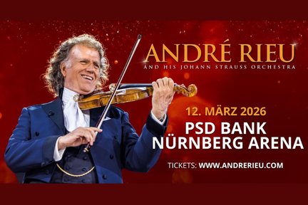 André Rieu lächelt, während er leidenschaftlich auf seiner Geige spielt, umgeben von einer festlichen roten Kulisse.