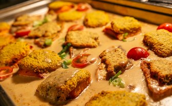 Ein Blech mit knusprigem Fischfilet, garniert mit Kirschtomaten und einer cremigen Sauce, serviert in einem Buffet-Stil.