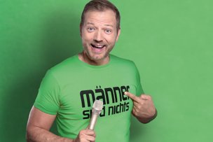 Mario Barth zeigt auf sein grünes Tour-Shirt mit grünem Hintergrund