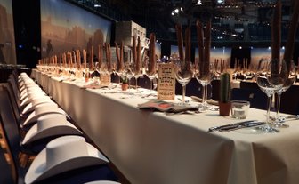 Lange Tafel mit eleganten Gläsern und rustikalen Dekorationen, die eine einladende Atmosphäre für eine Gala schafft.