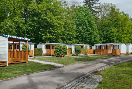 Eine Reihe von Mobilheimen in einem grünen Campingpark, umgeben von Bäumen und gepflegten Rasenflächen.