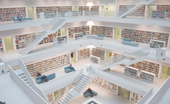 Eine moderne Bibliothek mit mehreren Etagen, die von hellen Regalen voller Bücher umgeben ist, bietet einen ruhigen Lesebereich.