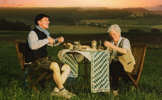 Tream mit einer älteren Dame an einem gedeckten Tisch auf dem Feld sitzend