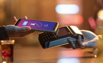 Ein Smartphone wird über ein Kartenlesegerät gehalten, während eine Zahlung getätigt wird, umgeben von einer warmen, einladenden Atmosphäre.