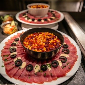 Ein appetitliches Arrangement aus Schinken, Oliven und einer würzigen Bohnensauce, das zum Genießen einlädt.