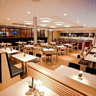 Die Innenansicht eines Restaurants zeigt leere Tische, stilvolle Sitzgelegenheiten und sanfte Beleuchtung.