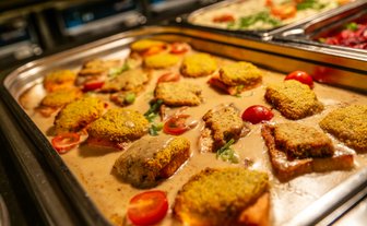 Ein Blech mit knusprigem Fischfilet, garniert mit Kirschtomaten und einer cremigen Sauce, serviert in einem Buffet-Stil.