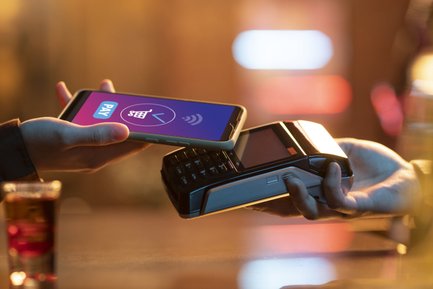 Ein Smartphone wird über ein Kartenlesegerät gehalten, während eine Zahlung getätigt wird, umgeben von einer warmen, einladenden Atmosphäre.