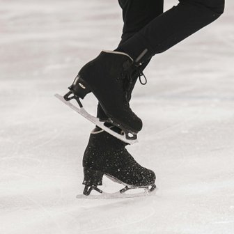 Ein Eiskunstläufer zeigt eine elegante Pose auf dem Eis, während seine schwarzen Schlittschuhe glänzen und die Kufen funkeln.