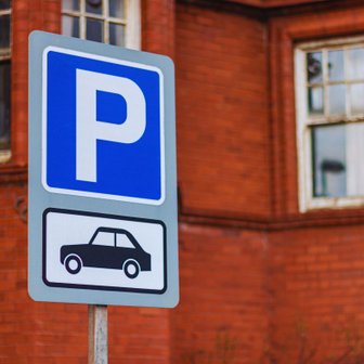 Ein blauer Parkplatzschild mit einem großen 'P' und einem Symbol eines Autos vor einer roten Backsteinmauer.