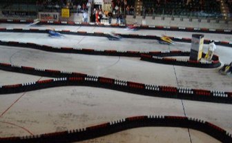 Eine Kartbahn mit kurvenreichen Strecken, auf der mehrere Karts in voller Fahrt unterwegs sind, umgeben von Zuschauern.