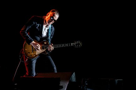 Joe Bonamassa auf der Bühne Gitarre spielend mit dunklem Hintergrund