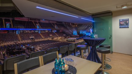 Die Aussicht von einer VIP-Lounge auf eine große, leere Arena, die mit Stühlen gefüllt ist und auf eine bevorstehende Aufführung wartet.
