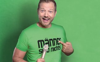 Mario Barth zeigt auf sein grünes Tour-Shirt mit grünem Hintergrund