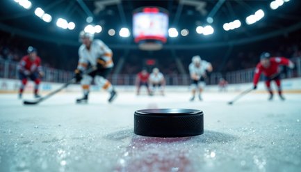 Der Fokus liegt auf einem Puck auf dem Eis, während Spieler in verschiedenen Trikots im Hintergrund agieren.