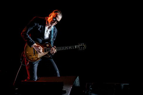 Joe Bonamassa auf der Bühne Gitarre spielend mit dunklem Hintergrund