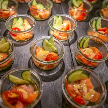 Ein Buffet mit Gläsern voller Lachs, begleitet von frischen Gurken und Kirschtomaten, ansprechend angerichtet.