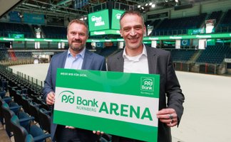 In der PSD Bank Arena präsentieren zwei Männer stolz ein Schild, das den Namen der Arena zeigt, umgeben von leeren Sitzplätzen.