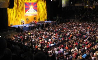 Eine große Menschenmenge versammelt sich in einer Halle, während eine Präsentation auf einer Bühne stattfindet.