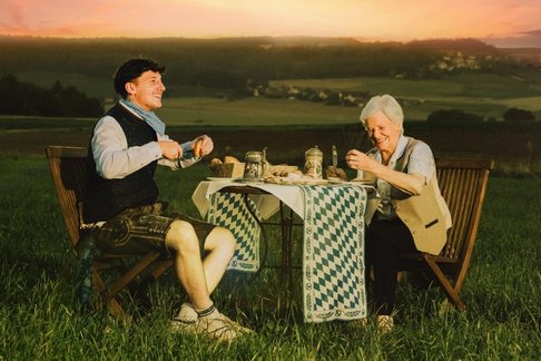 Tream mit einer älteren Dame an einem gedeckten Tisch auf dem Feld sitzend