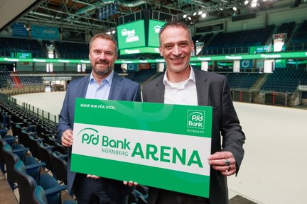 In der PSD Bank Arena präsentieren zwei Männer stolz ein Schild, das den Namen der Arena zeigt, umgeben von leeren Sitzplätzen.